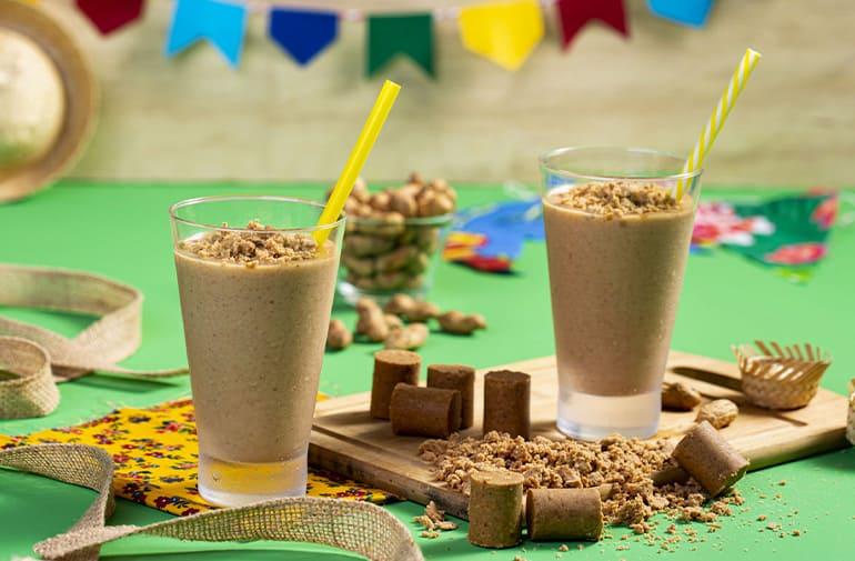 Dois copos de batida de paçoca à base de vodka, em uma mesa com paçoquinhas e decoração de festa junina