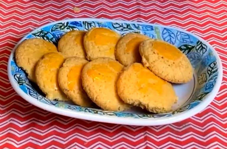 Broinhas de fubá de milho douradas, as broas estão em prato decorado com desenhos de folha, sobre uma toalha de festa junina