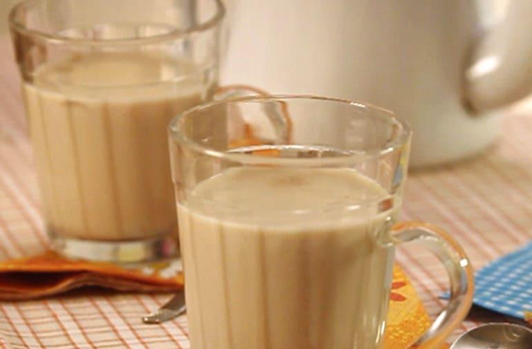 Duas xícaras grandes de vidro com chá de amendoim feito com leite condensado e canela, em mesa decorada de festa junina