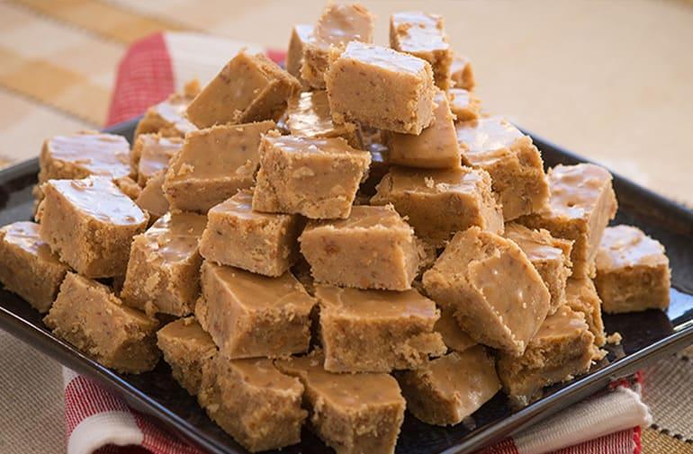 Cocada de amendoim com leite condensado, servida em cubos empilhados sobre um prato quadrado preto