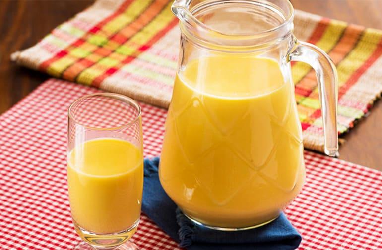 Jarra e copo de suco de milho com leite de soja sobre toalha quadriculada vermelha e branca