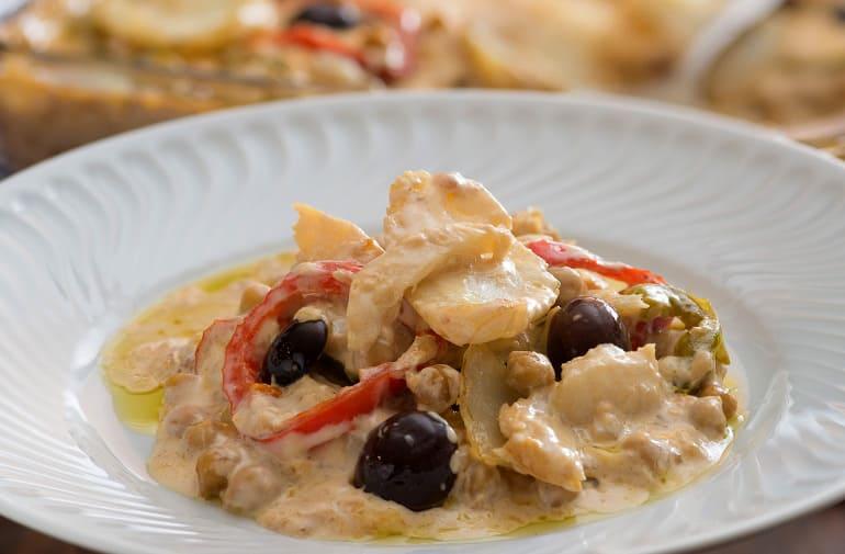 Postas de bacalhau cremoso, com batatas, pimentões, azeitonas e creme de cebola, servido em prato fundo branco