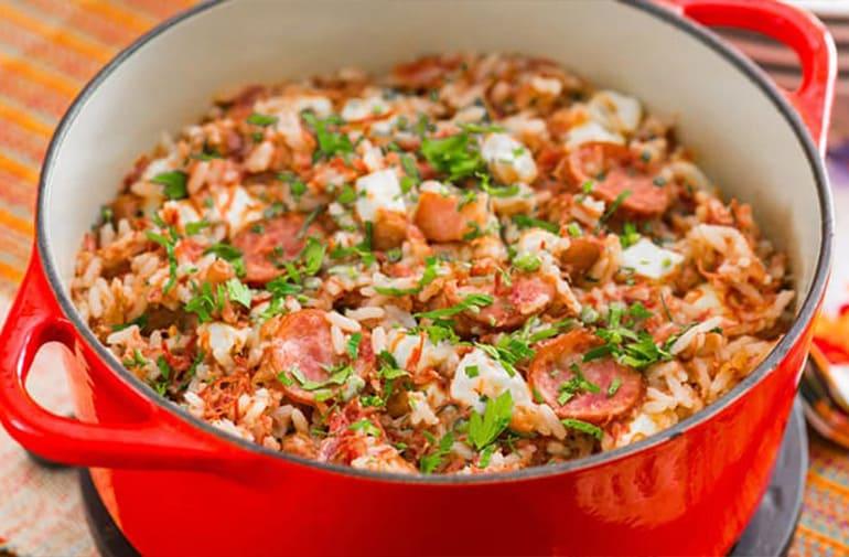 Baião de dois em panela vermelha, com arroz, linguiça, feijão, carne seca, bacon, coentro e outros ingredientes