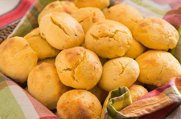 Broinhas de milho douradas, fofas e assadas, servidas em cesto decorado com pano xadrez típico de festa junina