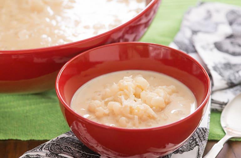 Canjica doce tradicional de milho, com leite condensado e coco, em potinho de sobremesa, ao lado de travessa maior.