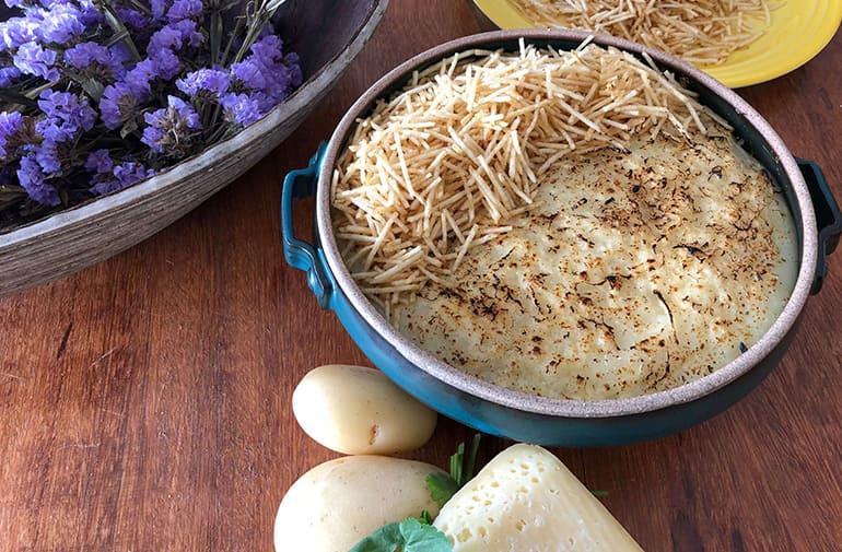 Escondidinho cremoso de queijo, coberto com batata palha crocante, servido em travessa rústica, em mesa com arranjos florais