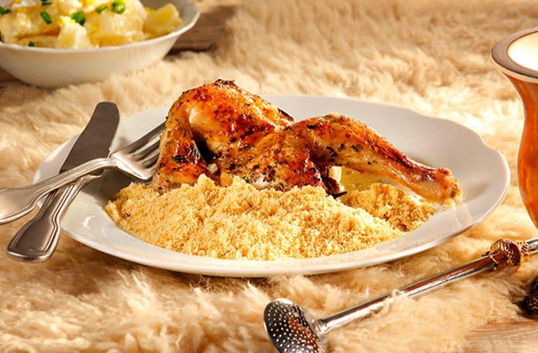 Galeto assado com limão e farofa, servido em prato branco, ao lado de cuia de chimarrão típica do Rio Grande do Sul