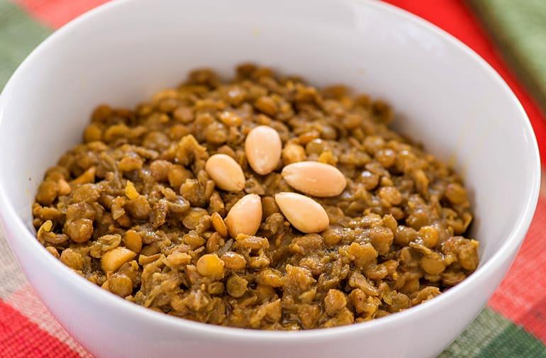 Tigela branca com lentilha refogada com amêndoas e especiarias, decorada com pedaços de amêndoa