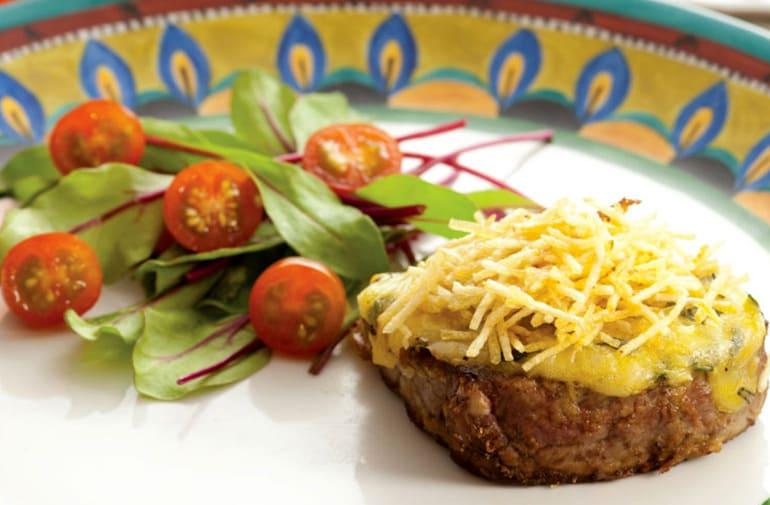 Medalhão de filé mignon com crosta de parmesão e batata palha, acompanhado de salada de folhas e tomate cereja em prato colorido