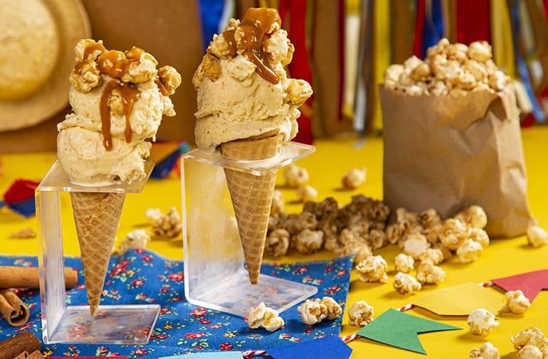 Casquinhas de sorvete de pipoca sabor churros, cercados por pipoca doce e decorações de festa junina