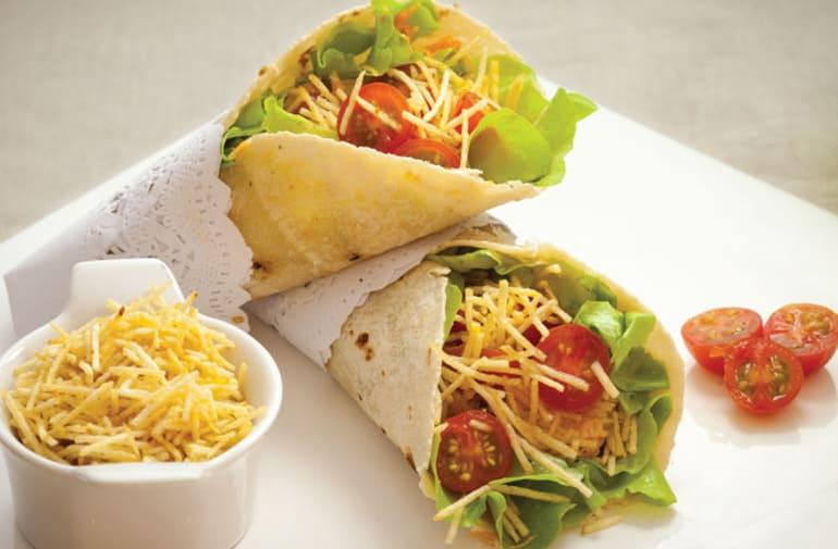 Receita prática de wrap com peito de peru, salada, tomate cereja, mussarela e batata palha, servida em um prato branco