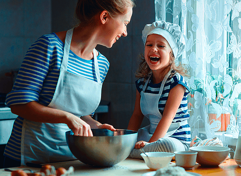 Adulta e criança estão numa cozinha e preparam receita de sobremesa caseira, em momento divertido